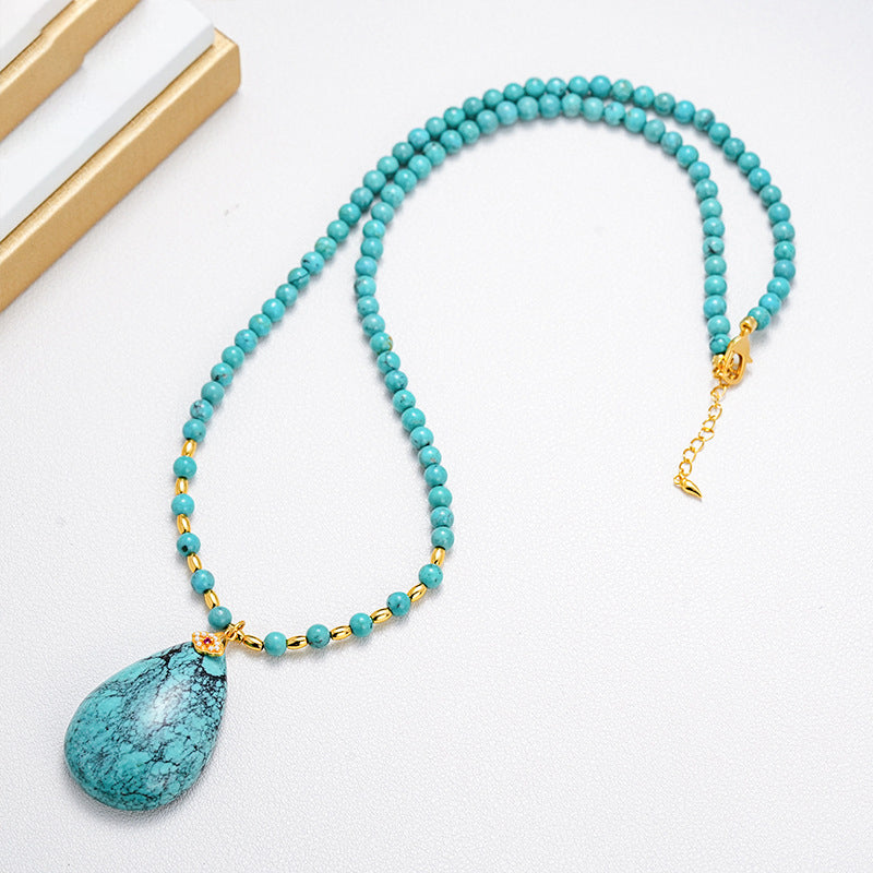 Turquoise gemstone necklace with gold plated beads and teardrop pendant on white background