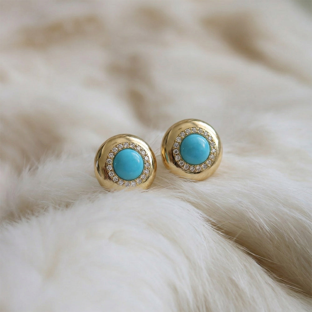 Gold plated stud earrings featuring round turquoise stones surrounded by small clear crystals on soft white fabric