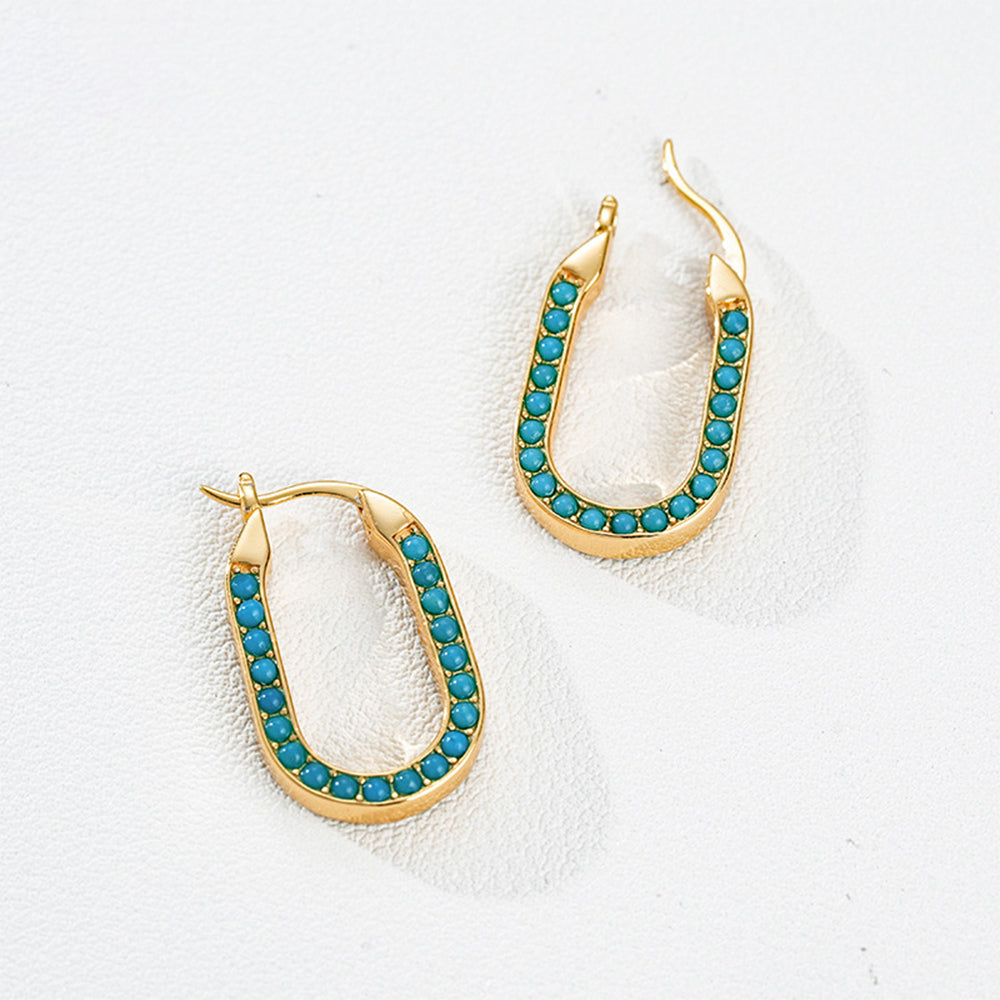 Gold plated oval hoop earrings with turquoise gemstones on white textured background