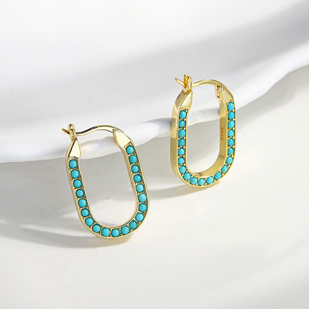 Gold-plated oval hoop earrings with small turquoise gemstones displayed on white surface