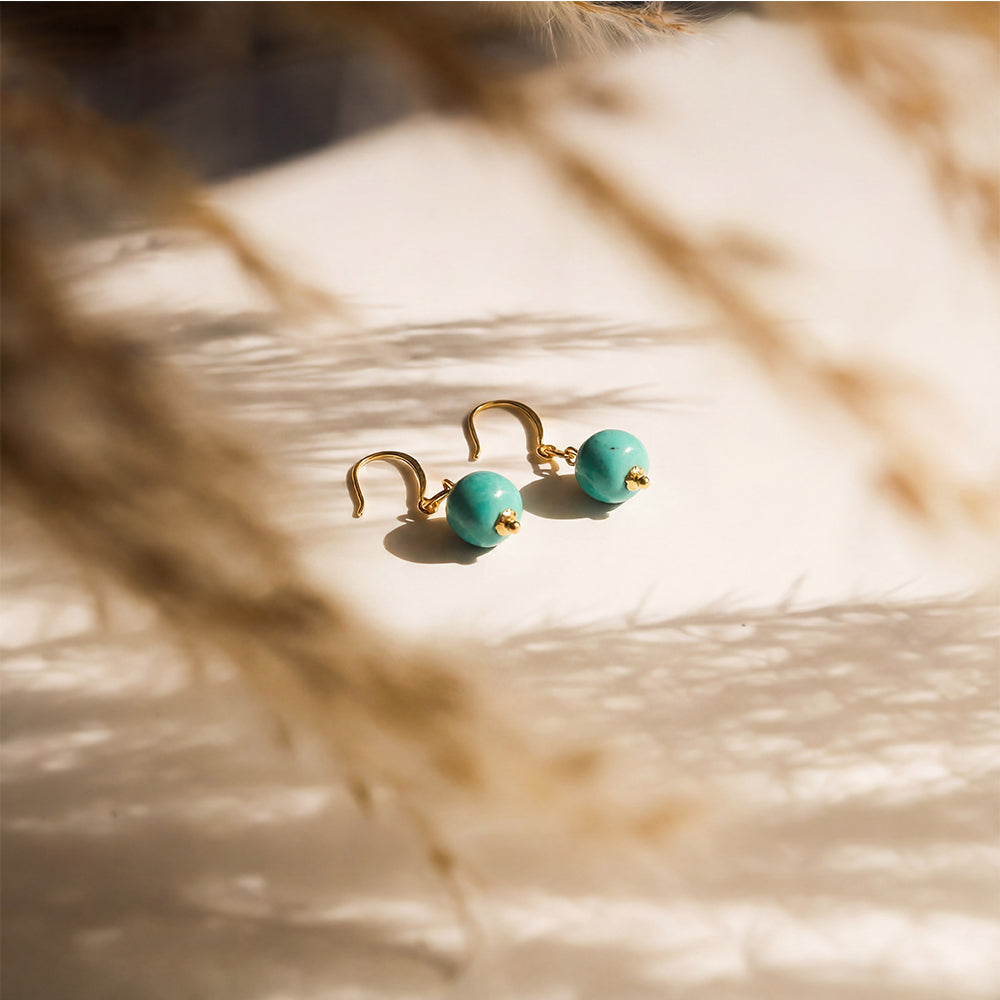 Gold-plated turquoise gemstone drop earrings on a white surface with soft shadows