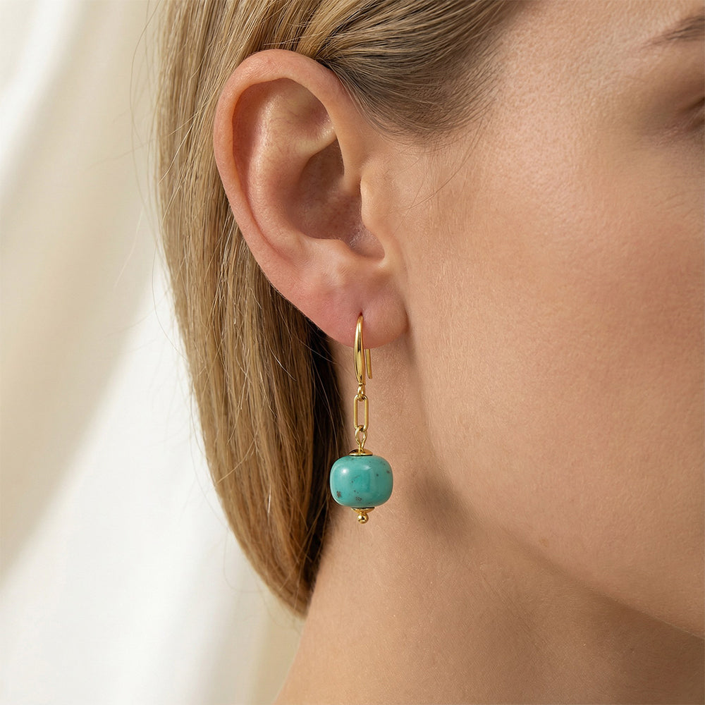 Close-up of a woman's ear wearing a gold-plated earring with a natural turquoise gemstone bead