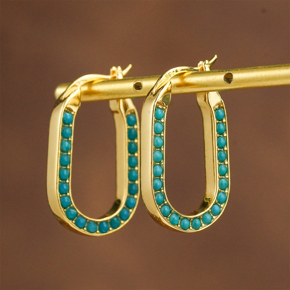 Gold plated oval hoop earrings adorned with small turquoise gemstones on a beige background