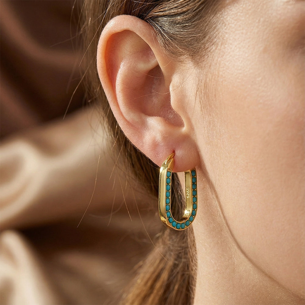 Close-up of gold-plated hoop earring with turquoise gemstone inlay worn on ear