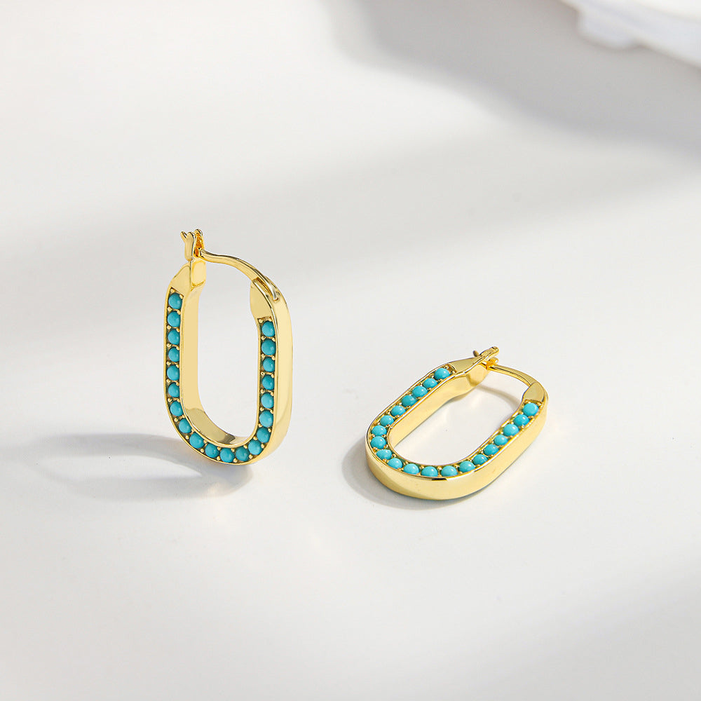 Gold plated rectangular hoop earrings with turquoise gemstone beads on white surface