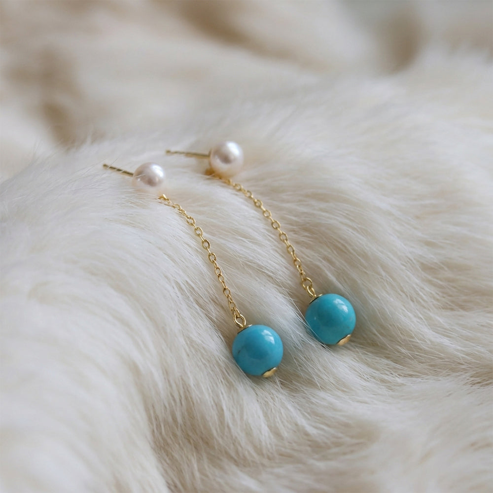 Gold-plated chain earrings with turquoise gemstone beads and pearl studs on soft white fur background