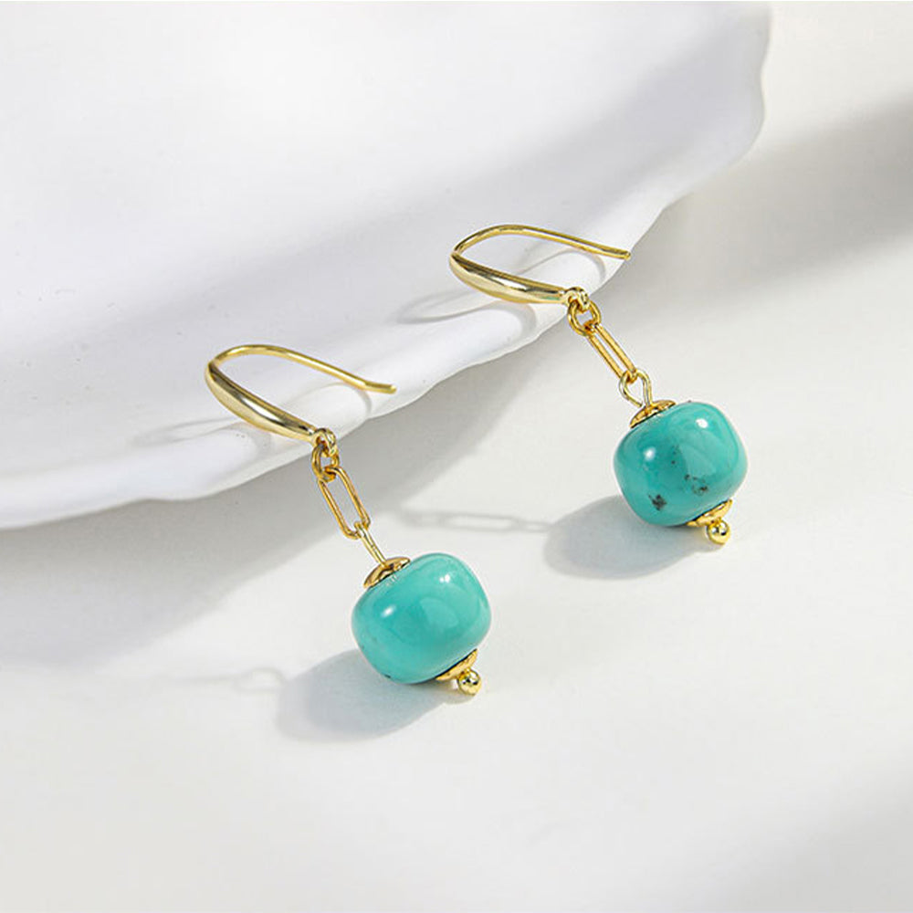Gold-plated dangle earrings with natural turquoise gemstone beads on white surface