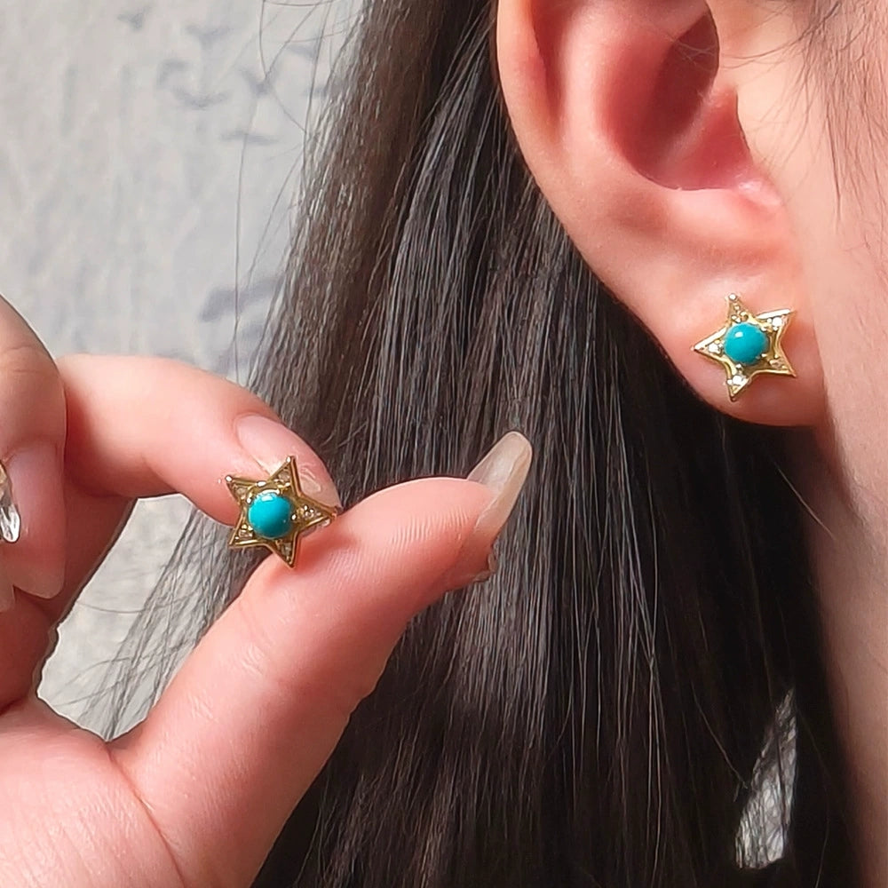 Close-up of turquoise star-shaped gold plated stud earrings worn and held near ear with dark hair background