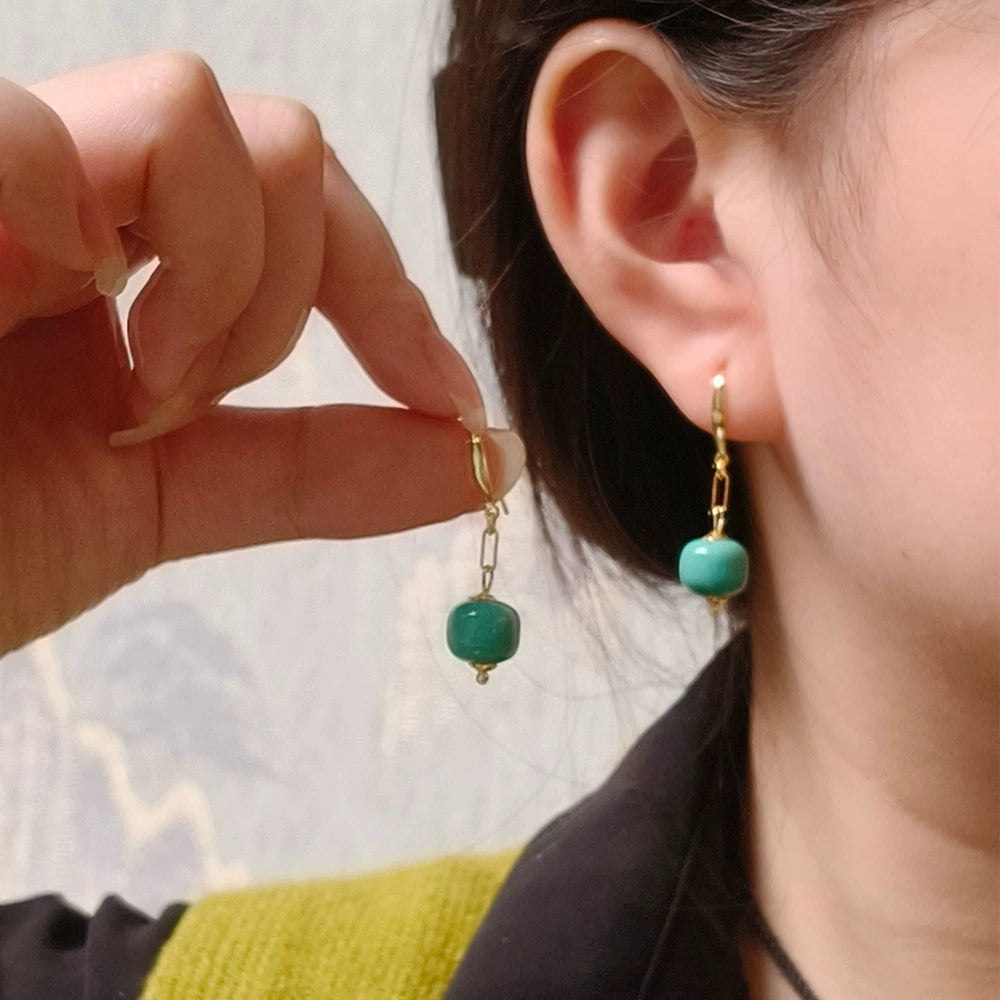 Close-up of gold-plated hoop earrings with green turquoise gemstone beads worn and held by a woman