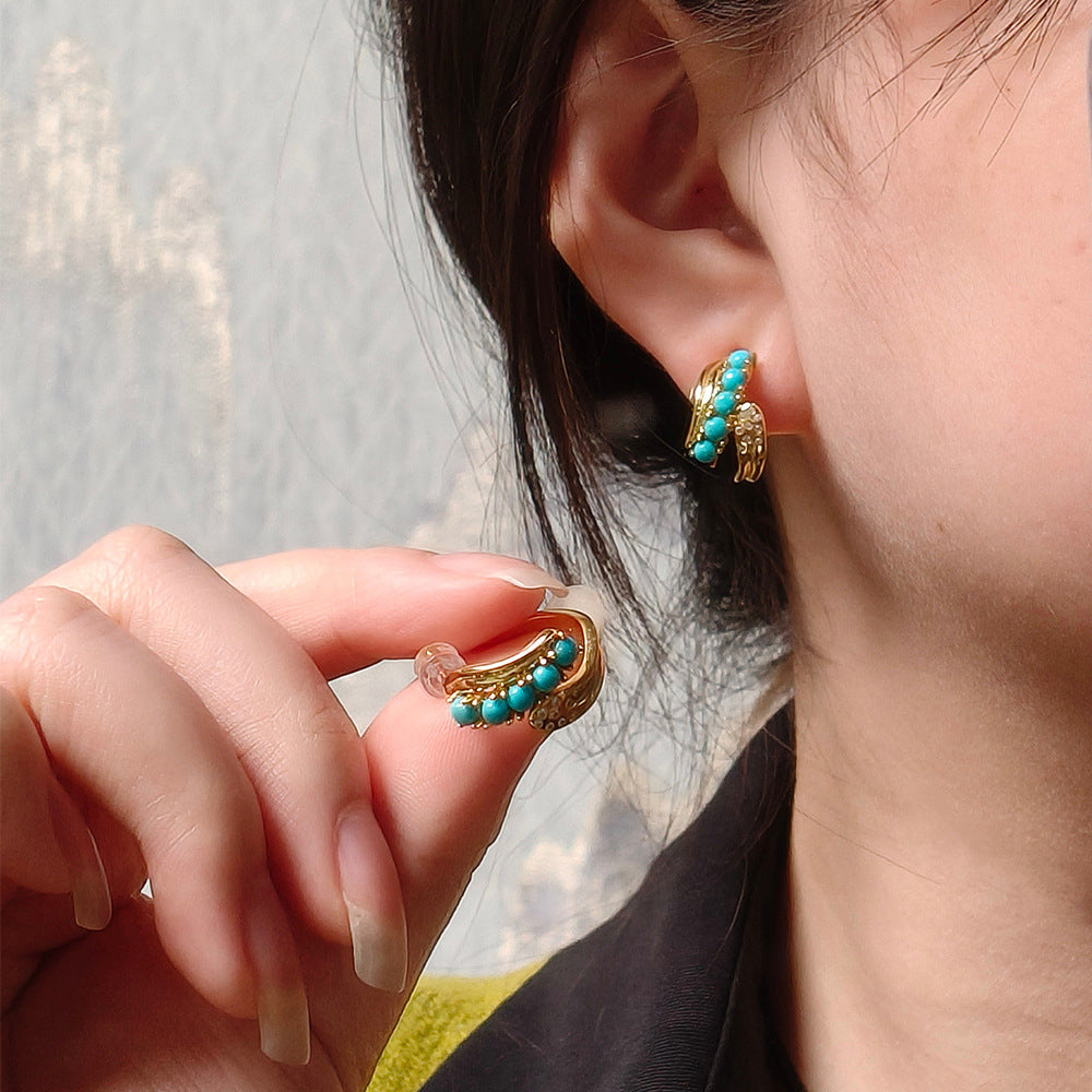 Close-up of hand holding gold-plated turquoise gemstone earring worn on ear, natural jewelry detail