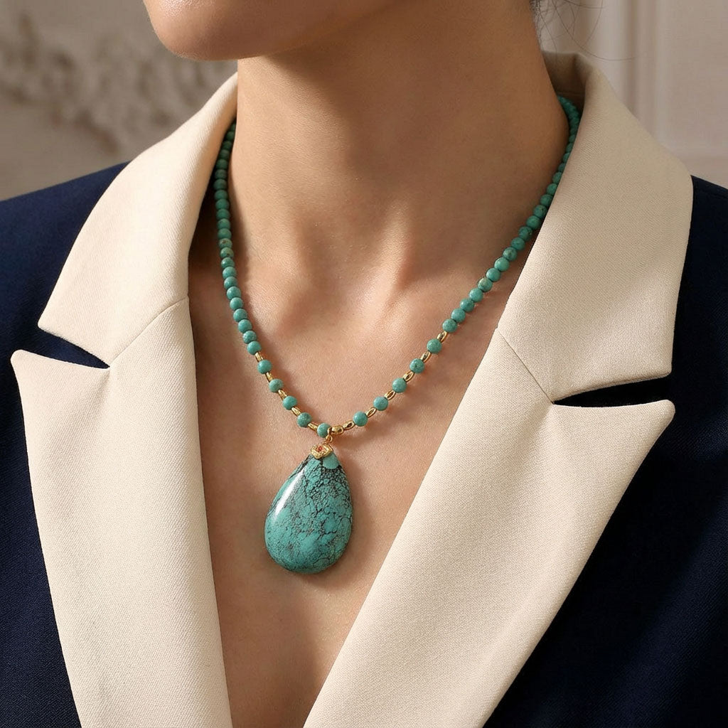 Close-up of a woman wearing a turquoise beaded necklace with a large teardrop pendant, paired with a beige and navy blazer