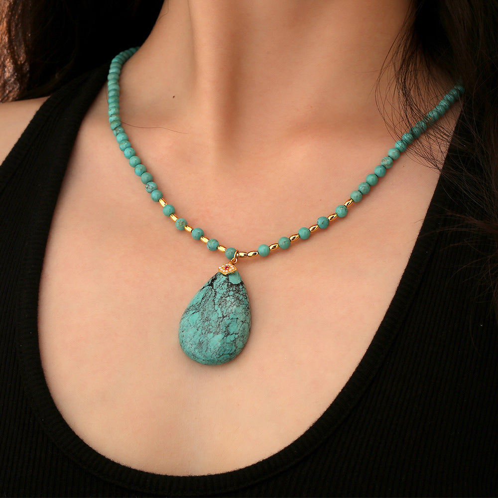 Close-up of a turquoise beaded necklace with a teardrop pendant worn on a woman in a black top