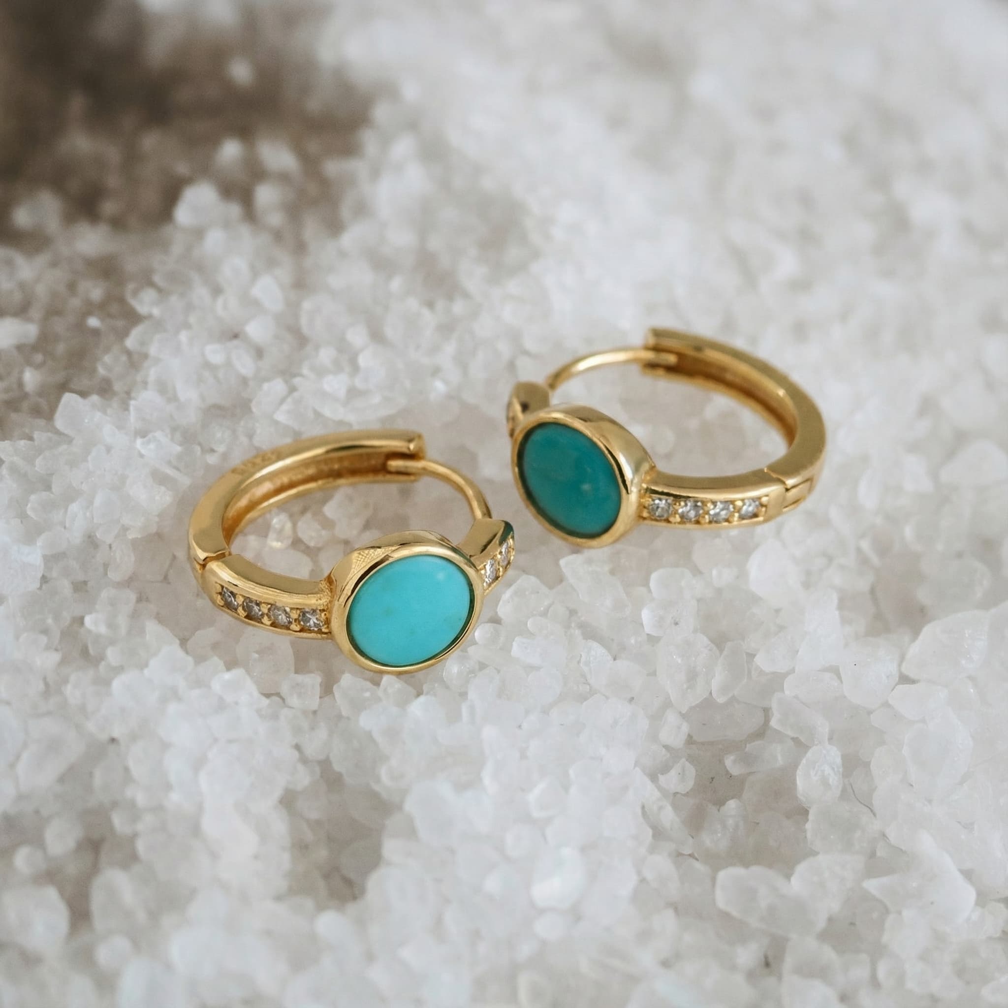 Gold plated hoop earrings with turquoise stones and small clear crystals on white crystal background