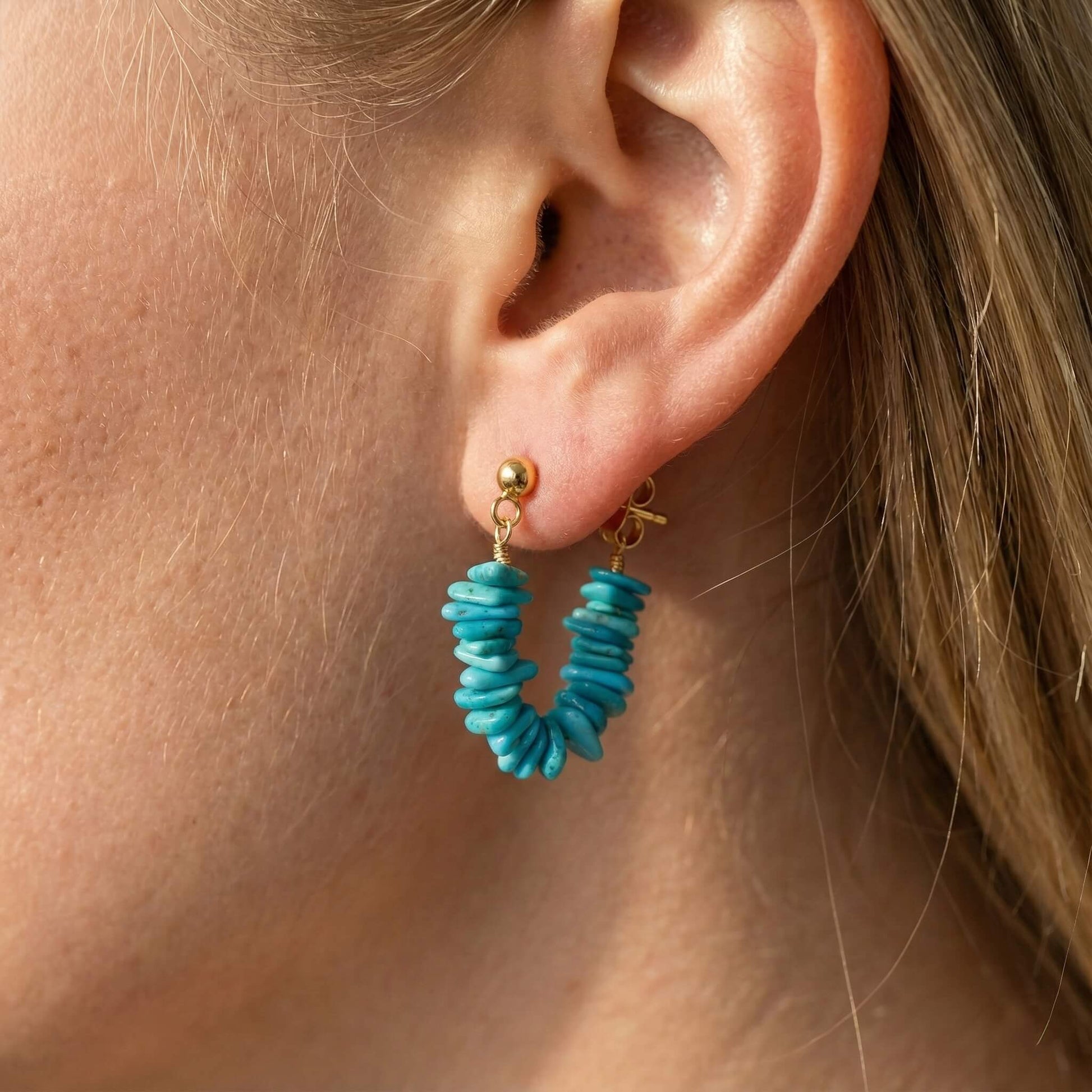 Close-up of a woman's ear wearing gold-plated hoop earrings made of stacked turquoise gemstone beads