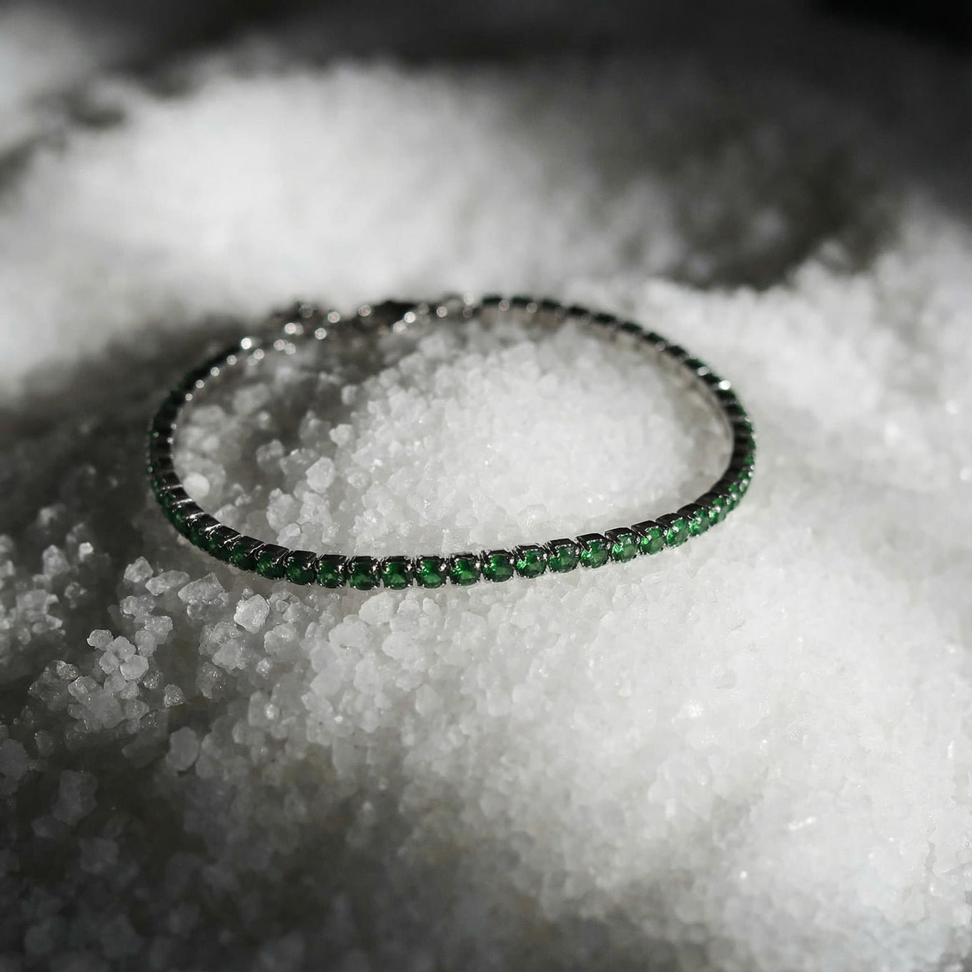 Green gemstone tennis bracelet with silver setting, displayed on coarse white salt crystals
