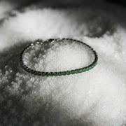 Green gemstone tennis bracelet with silver setting, displayed on coarse white salt crystals