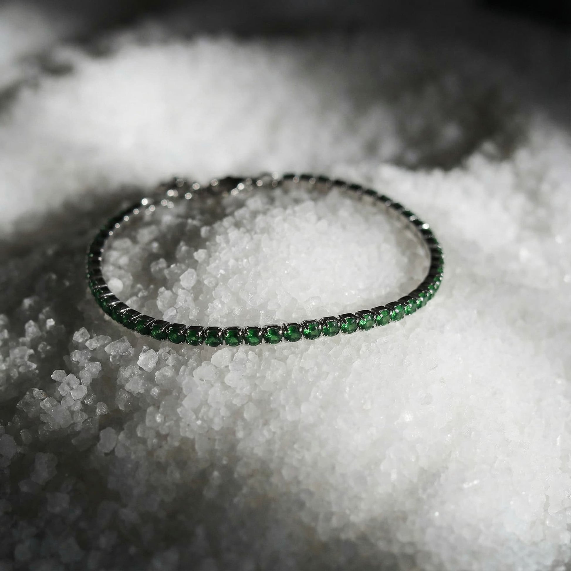 Green gemstone tennis bracelet with silver setting, displayed on coarse white salt crystals