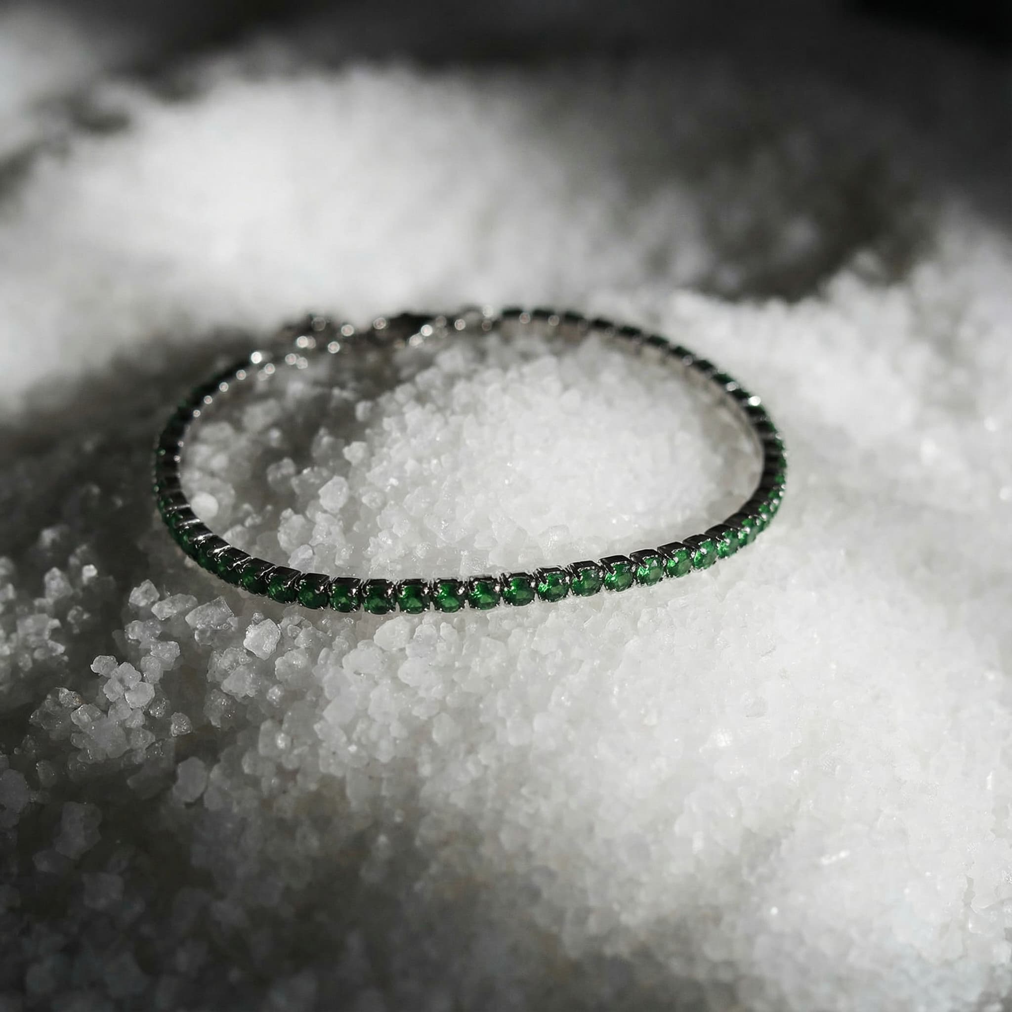 Green gemstone tennis bracelet with silver setting, displayed on coarse white salt crystals