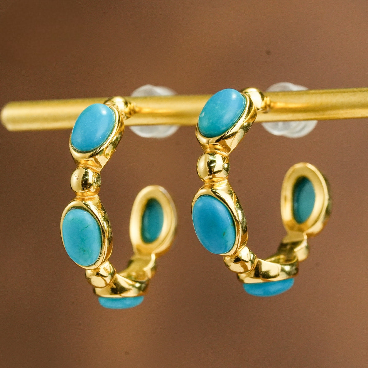 Gold-plated hoop earrings with oval turquoise gemstones displayed on a gold rod