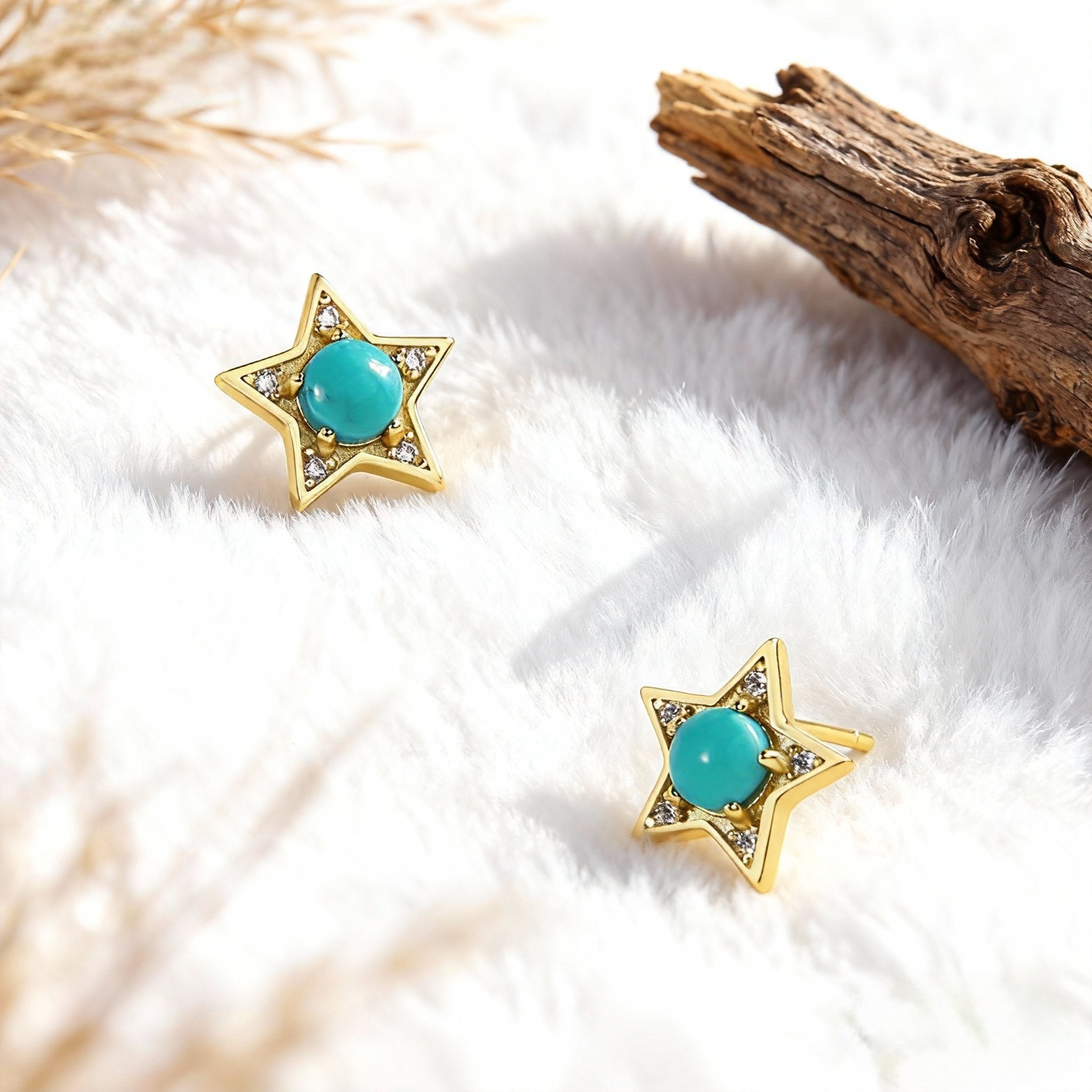 Gold star-shaped earrings with turquoise stones and small crystals on white fur background with driftwood