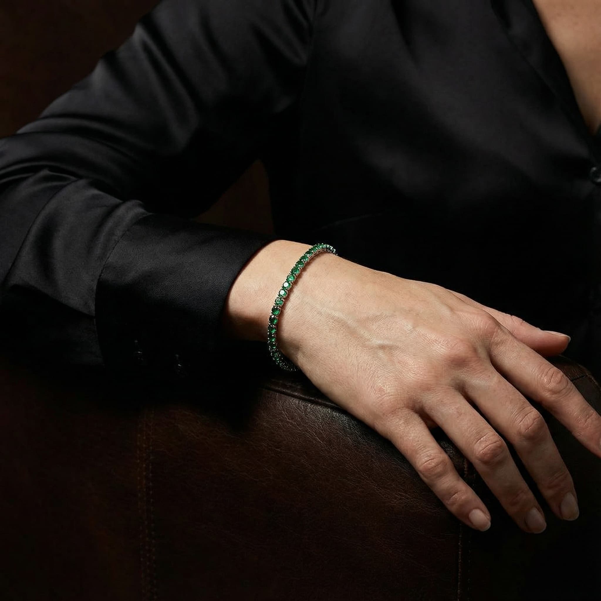 Close-up of a hand wearing a gold plated bracelet with green gemstones, styled with a black satin shirt