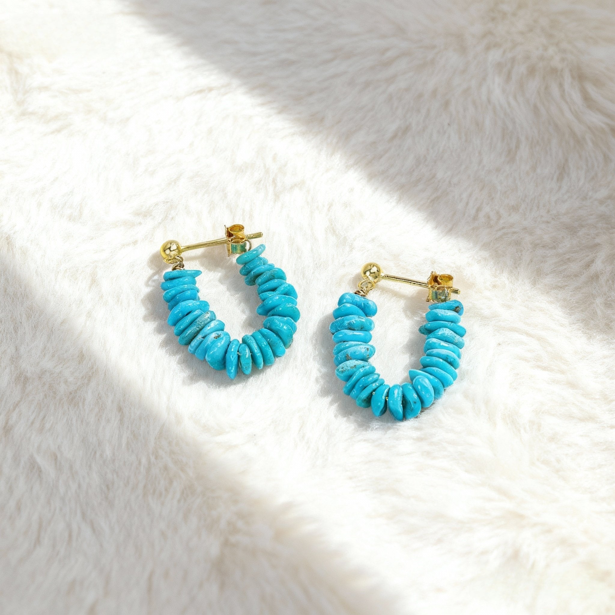 Pair of turquoise gemstone hoop earrings with gold plated studs on soft white fabric background