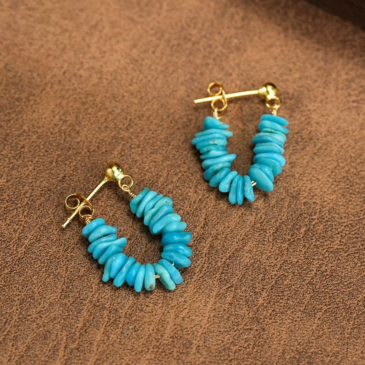 Gold plated stud earrings with stacked turquoise gemstone chips on brown textured surface