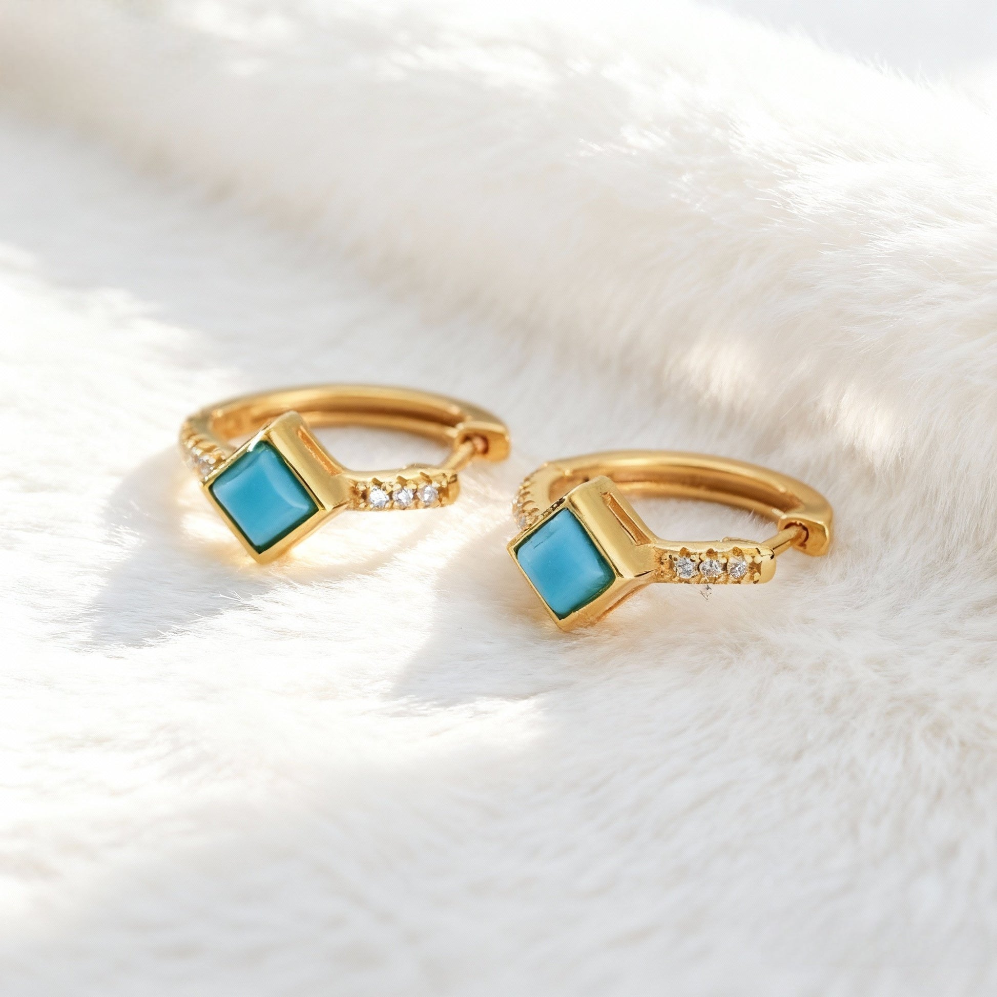Gold plated hoop earrings with square turquoise stones and small diamonds on white fur background