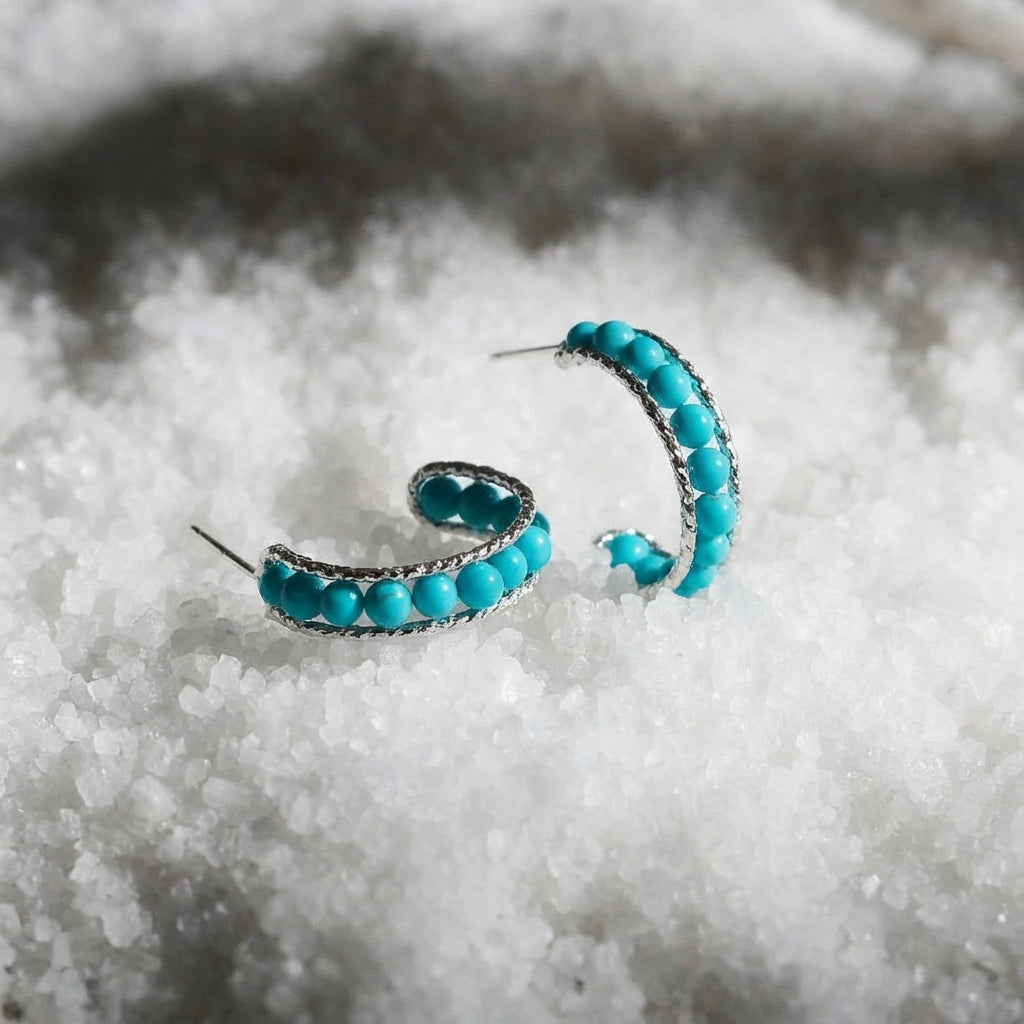 Silver hoop earrings with turquoise beads on white crystalline surface