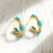 Gold plated hoop earrings with oval turquoise gemstones on white fur background