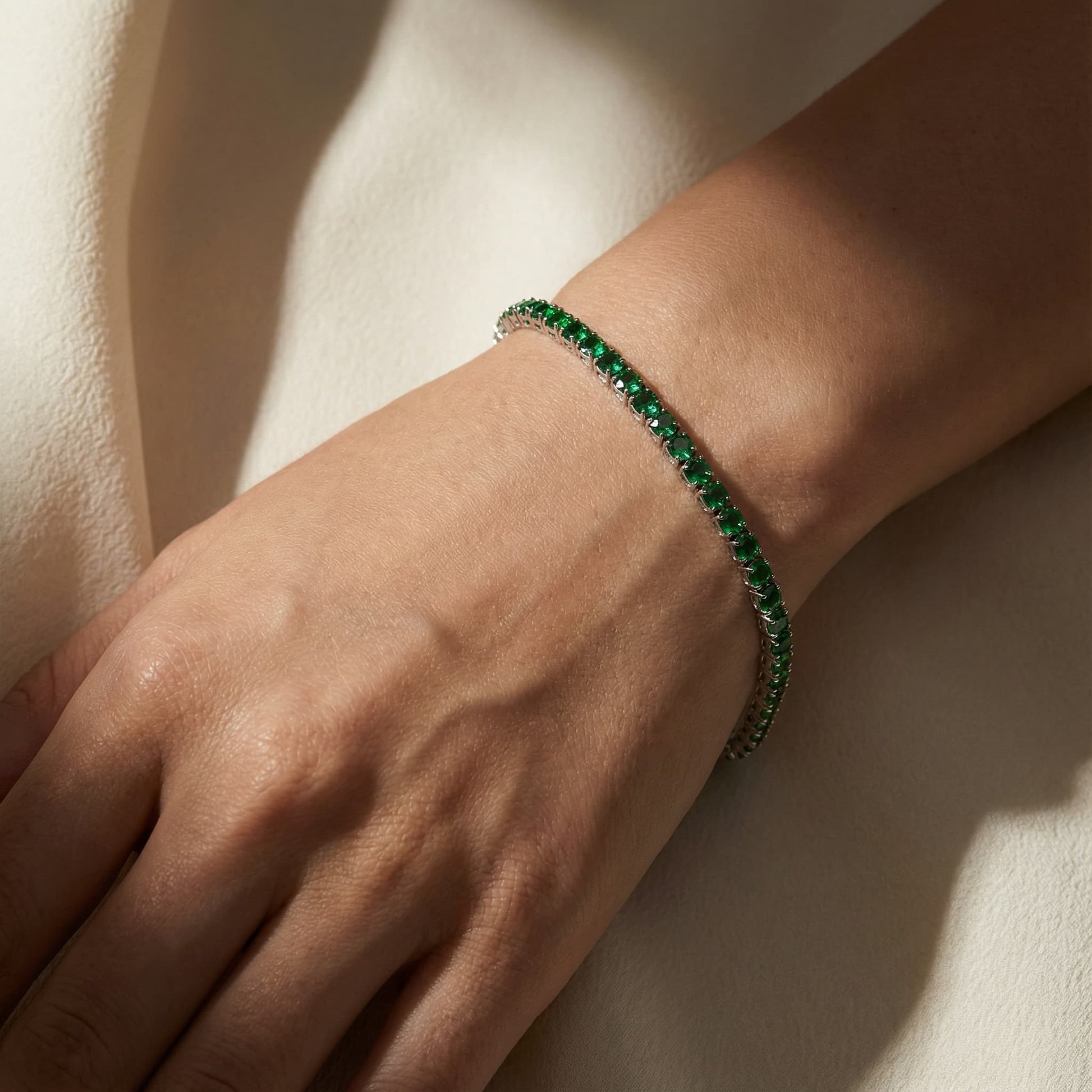 Close-up of a wrist wearing a gold plated bracelet with vivid green gemstones, elegant natural jewelry style