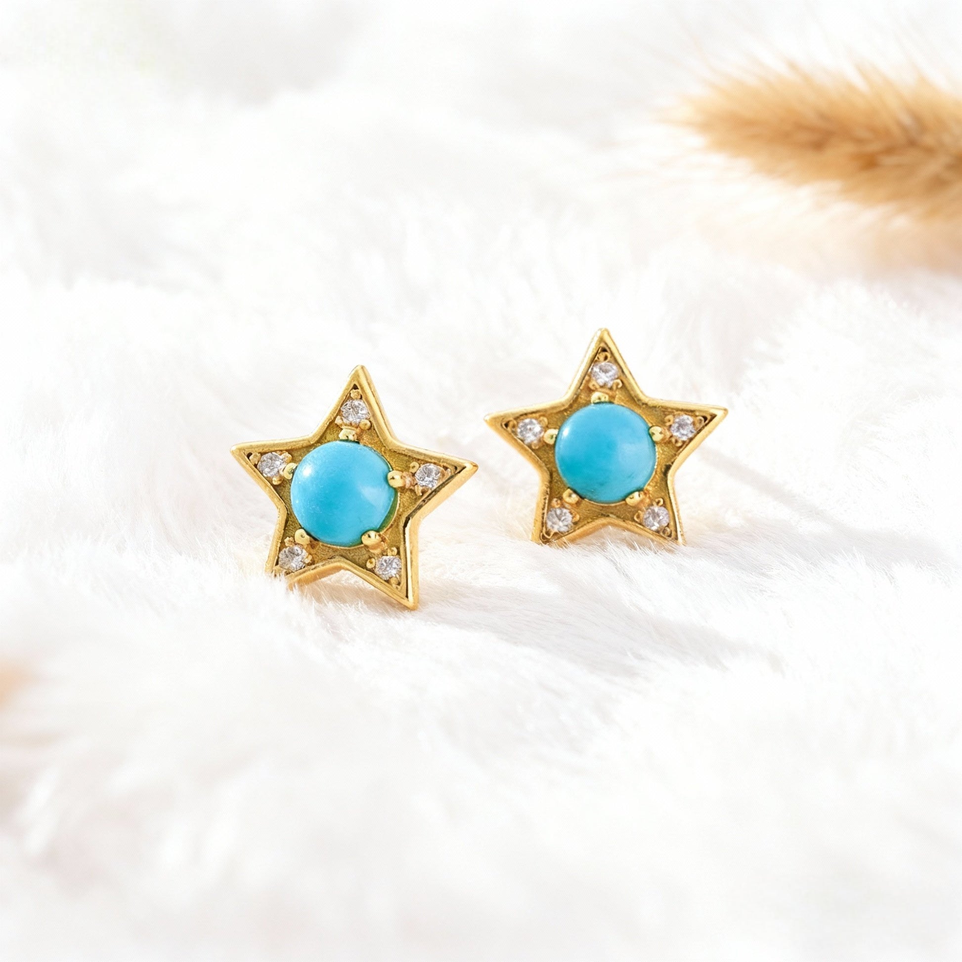 Gold plated star-shaped earrings with turquoise center and small clear gemstones on white soft fabric