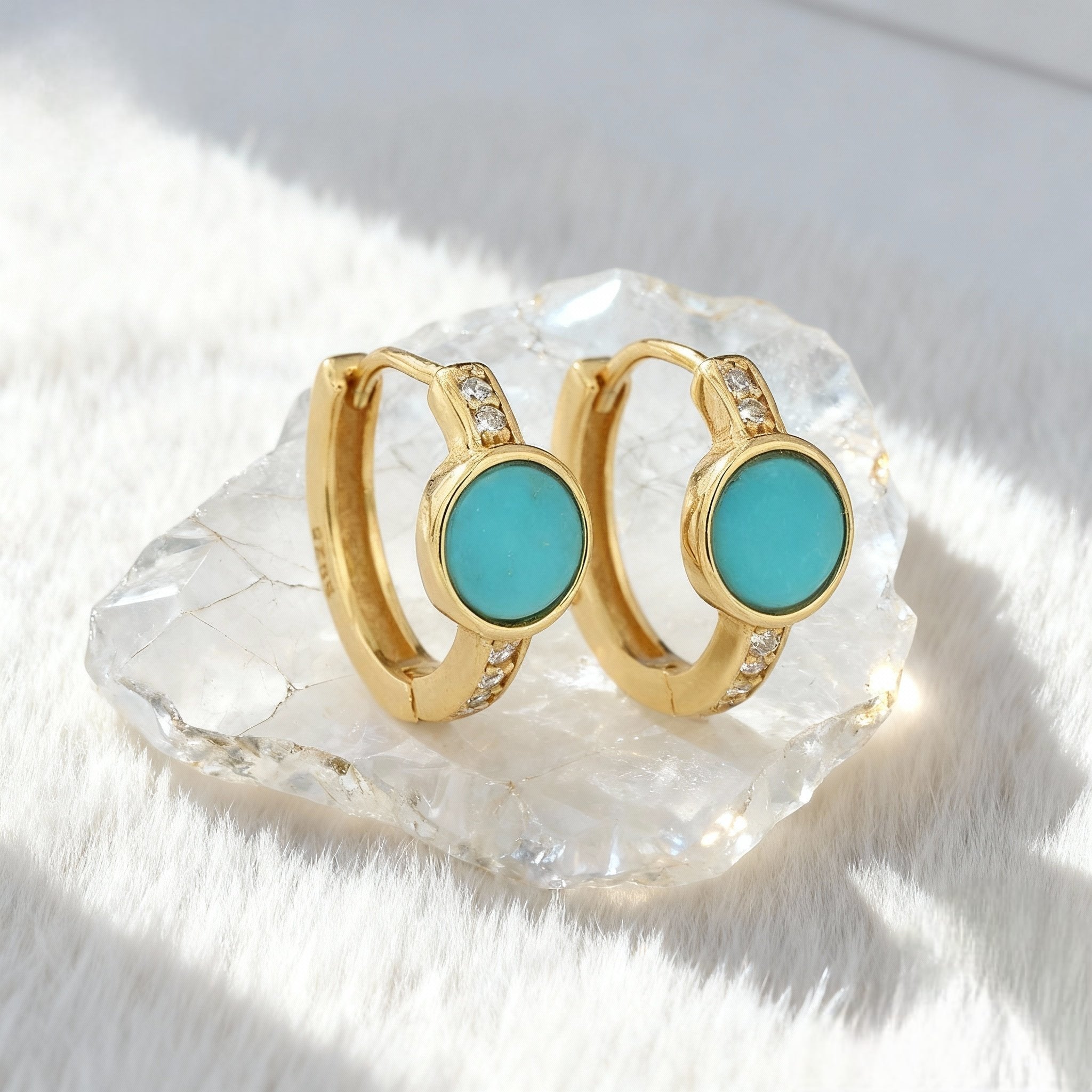 Gold plated hoop earrings with round turquoise stones and small clear gemstones, displayed on a clear crystal