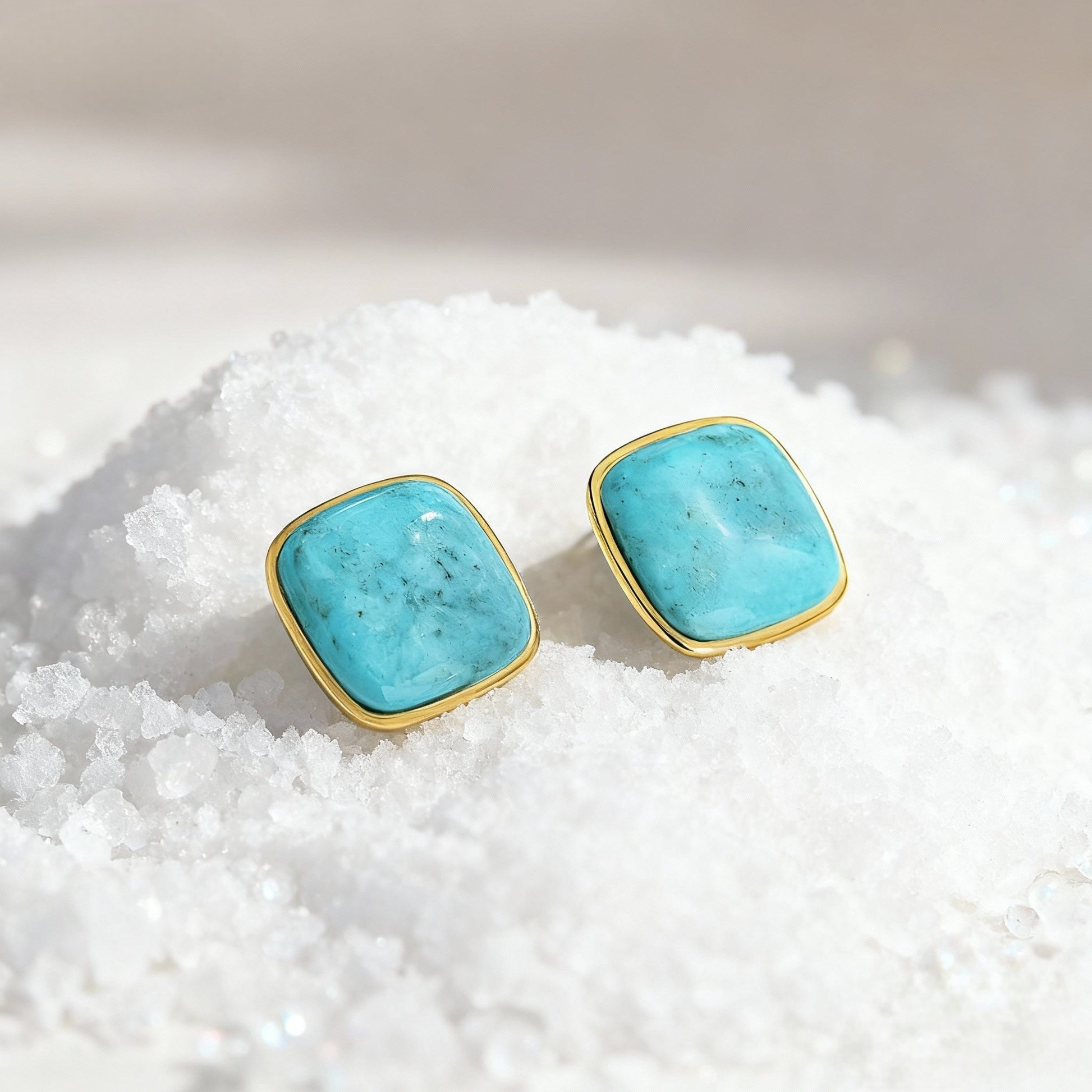 Turquoise gemstone stud earrings with gold plated setting on white crystal surface